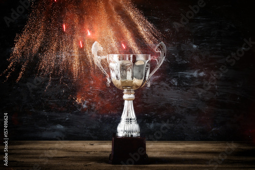 low key image of trophy over wooden table and dark background, with abstract fireworks.