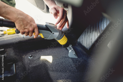 Professional detailer vacuuming carpet of car interior, using steam vacuum photo