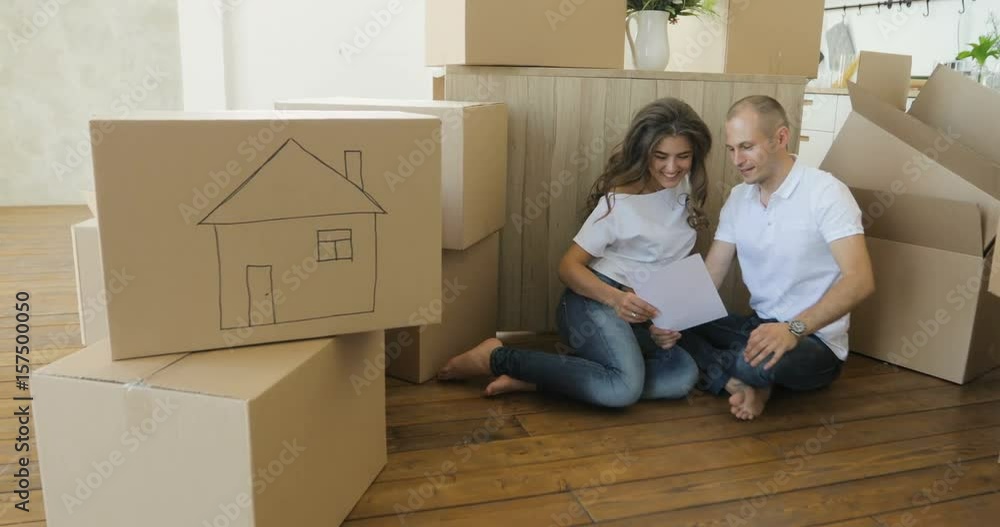 Couple planning their new living room siting on the floor. young family moving to a new apartment and carrying boxes Couple planning their new living room siting on the floor. young family moving to a new apartment and carrying boxes