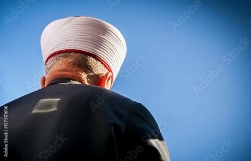 Muslim cleric seen from his back with a blue sky background. An editorial illustration for Ramadan fast, Muslim prayer, Islamic piety, interfaith dialogue, prayer to God, abstract  Ramadan concept.