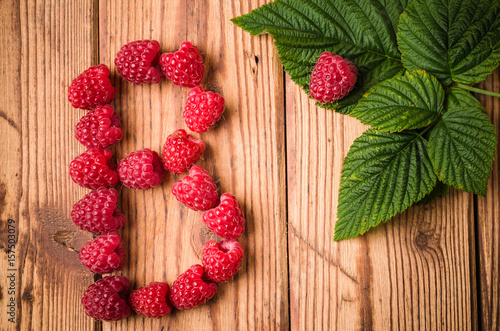 Letter B of raspberries with leaves on a wooden surface, close-up