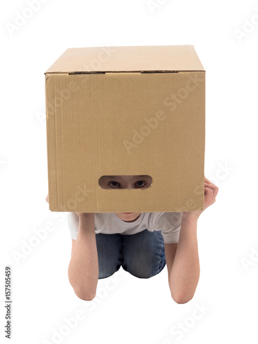 Little girl in a white T-shirt and jeans hides in a box and peeks through a slot on a white background
