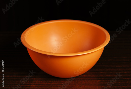 Orange cup stands alone on a wooden table on a black background. Subject photography of kitchen utensils..