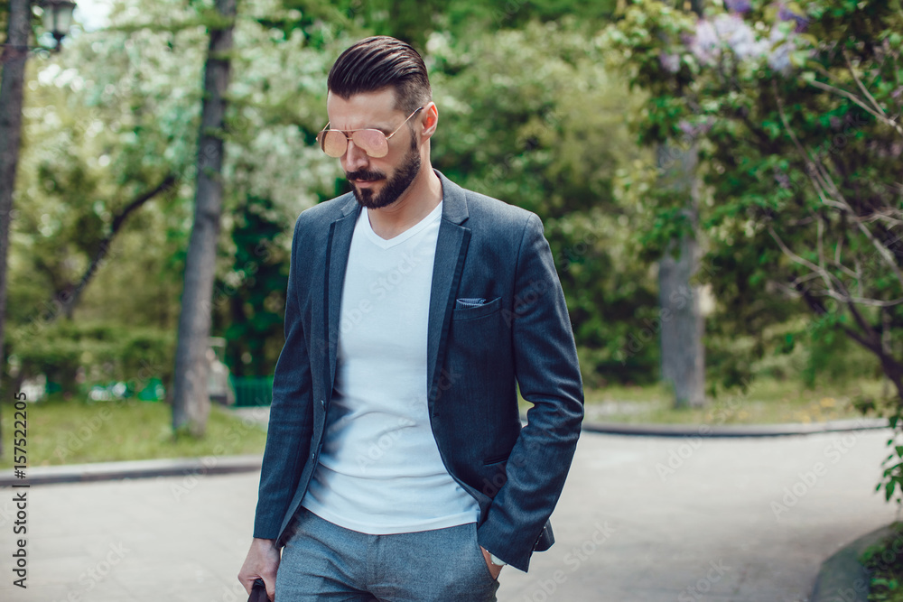 Stylish man with a beard and in sunglasses standing in the park. Stylish man with a beard and in sunglasses standing in the park.