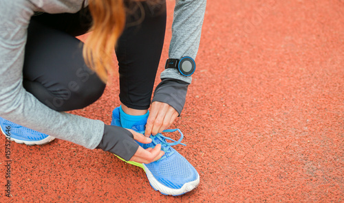 Athletic woman with smart watch on running track tying shoe laces