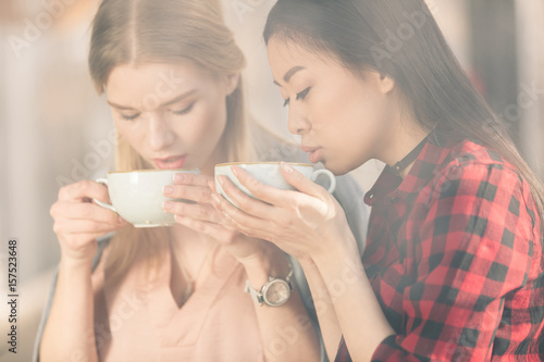 Beautiful young women holding white cups and drinking fresh coffee, coffee break concept