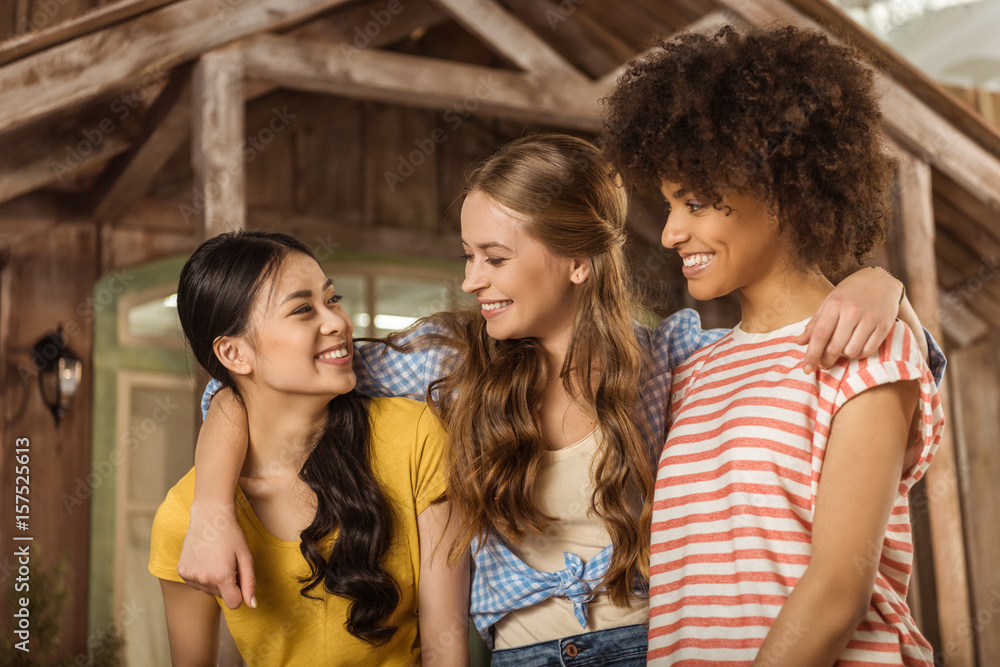 Multiethnic group of beautiful smiling young women standing embracing on porch