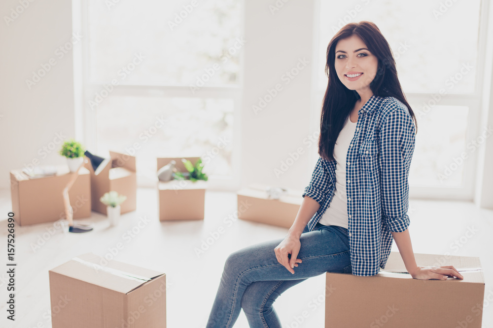 Home, sweet home! Young cute girl in casual clothes is sitting on the box with her belongings in the new light modern apartment. She just moved in, A lot of unpacked boxes near her Home, sweet home! Young cute girl in casual clothes is sitting on the box with her belongings in the new light modern apartment. She just moved in, A lot of unpacked boxes near her
