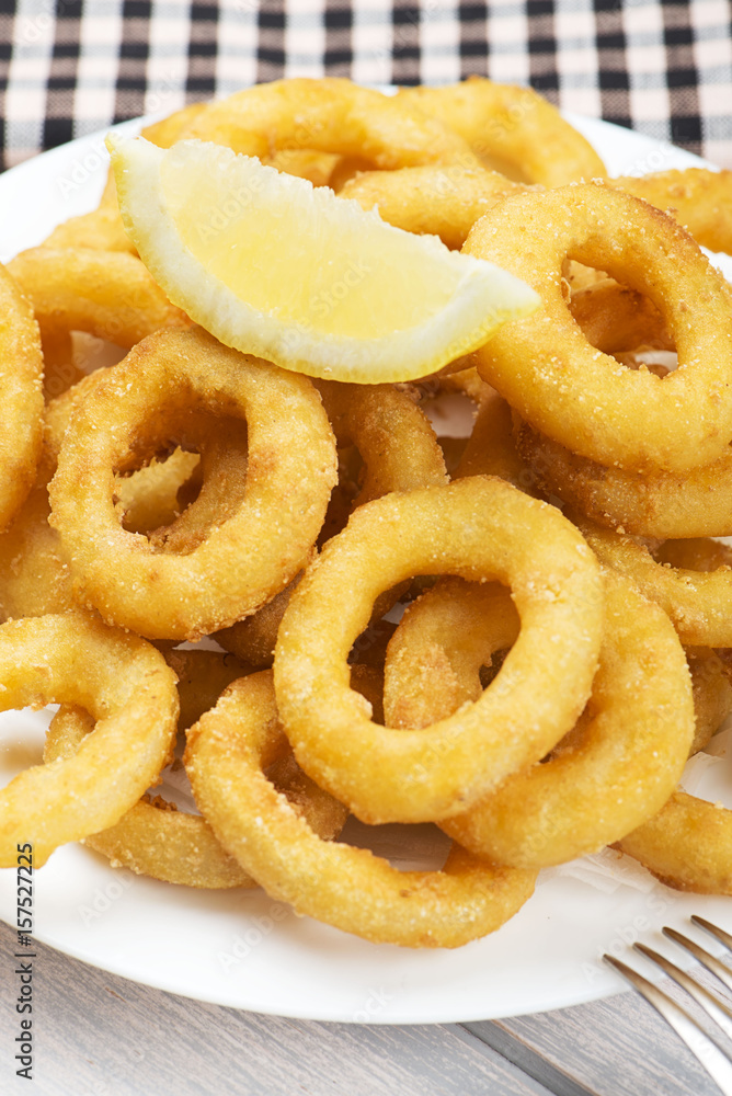 Close-up of platter of squid to la romana and a lemon on white wooden table. Squids. Vertical shoot. Close-up of platter of squid to la romana and a lemon on white wooden table. Squids. Vertical shoot.