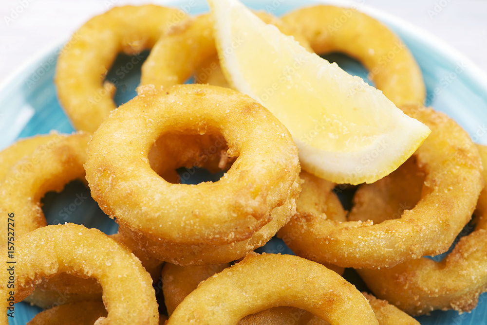 Close-up of a plate of squids a la romana and a lemon on blue plate. Squids. Horizontal shoot. Close-up of a plate of squids a la romana and a lemon on blue plate. Squids. Horizontal shoot.