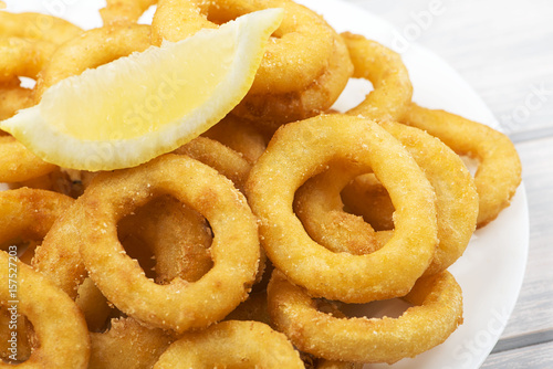 Close-up of platter of squid to la romana and a lemon on white wooden table. Squids.