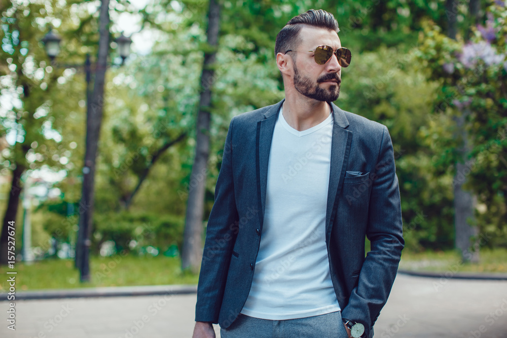 Stylish man with a beard and in sunglasses standing in the park.