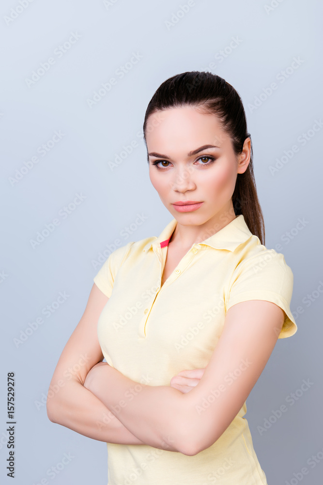 Portrait of serious young freelancer brunette lady, she stands with crossed hands in yellow tshirt on pure light background. So severe and strict Portrait of serious young freelancer brunette lady, she stands with crossed hands in yellow tshirt on pure light background. So severe and strict