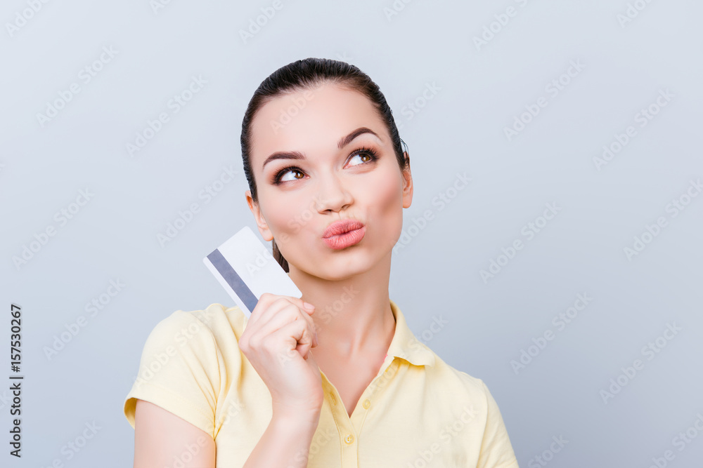 So easy! Playful brunette hot girl is thinking of online shopping in internet. She is in casual clothes, standing on a pure light background, holding a credit card So easy! Playful brunette hot girl is thinking of online shopping in internet. She is in casual clothes, standing on a pure light background, holding a credit card