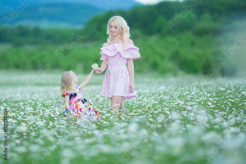 Blond mother with cute little daughter wearing white colourful pink dresses in chamomile field, summer time Enjoying spending time together happy childhood photo