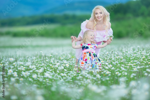 Blond mother with cute little daughter wearing white colourful pink dresses in chamomile field, summer time Enjoying spending time together happy childhood photo