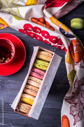Colorful macaroons in a gift box and fruit tea on wooden background. Top view