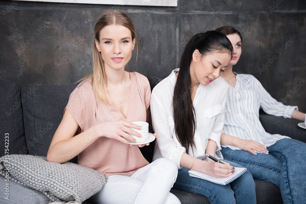 asian girl writing at notebook while her friends drinking coffee while sitting on sofa asian girl writing at notebook while her friends drinking coffee while sitting on sofa