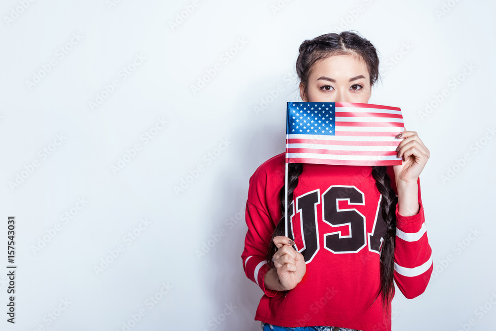 Beautiful asian girl in patriotic outfit holding american flag and looking at camera Beautiful asian girl in patriotic outfit holding american flag and looking at camera