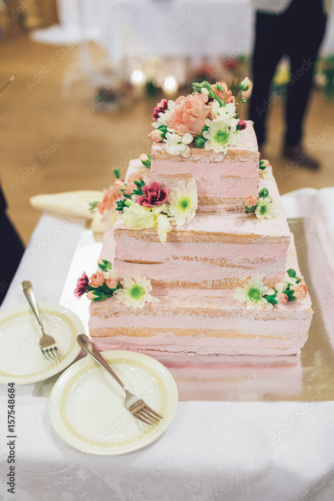 Fototapeta premium Square tired wedding cake decorated with pink flowers and pink cream