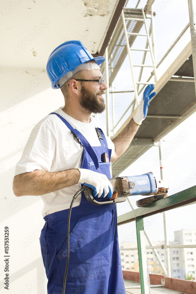 Uśmiechnięty pracownik budowlany w stroju roboczym i w kasku macha ręką na przywitanie. Uśmiechnięty pracownik budowlany w stroju roboczym i w kasku macha ręką na przywitanie.