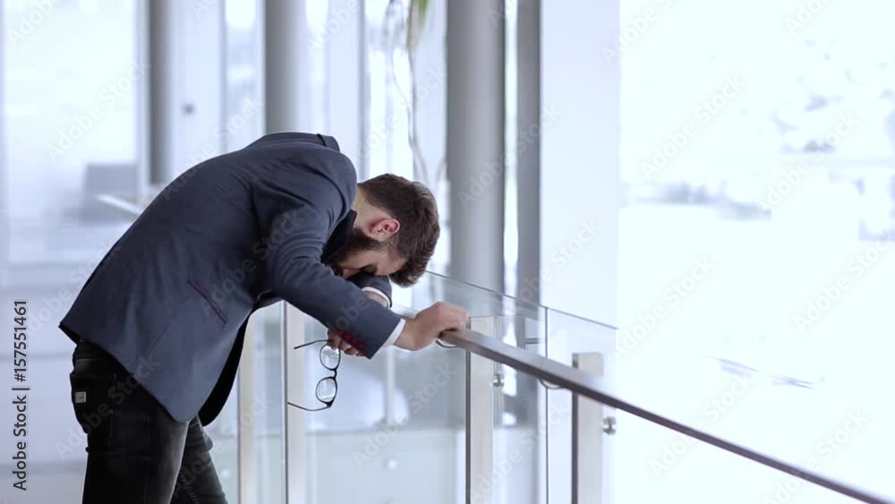Depresed businessman bended over fence in company building and having problems Depresed businessman bended over fence in company building and having problems