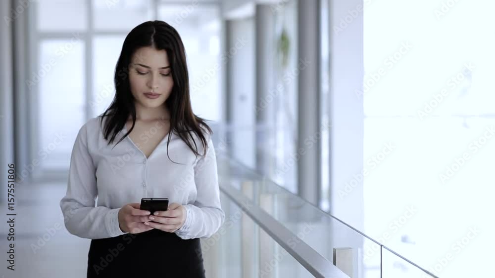 Woman standing and typing on her mobile phone in business building Woman standing and typing on her mobile phone in business building
