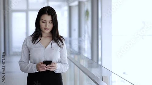 Woman standing and typing on her mobile phone in business building photo