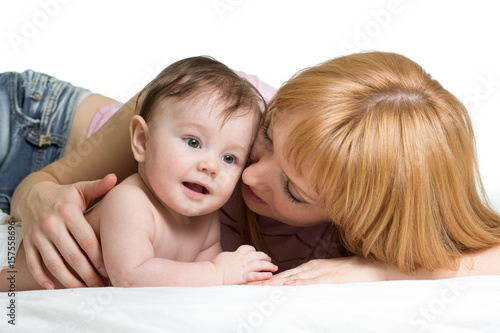 Cute mother embraces her little baby. Woman and newborn kid boy relax in a white bedroom.