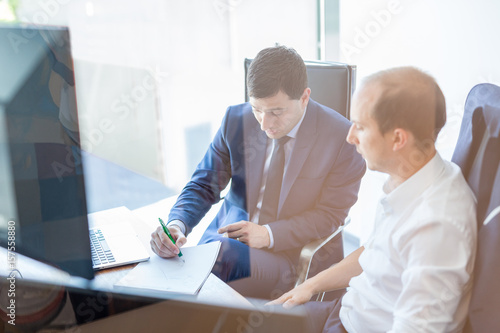 Image of two corporate businessmen discussing a bisiness problem at meeting in modern trading office. Businesspeople sitting at the boardroom and discussing business-plan. photo