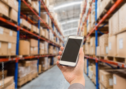 Warehouse storage of retail merchandise shop. Businessman checking inventory in stock room of a manufacturing company on smartphone 