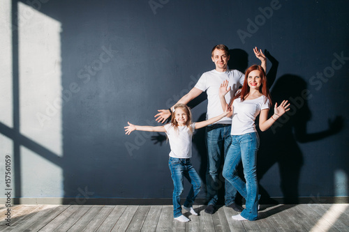 Happy family portrait standing on gray background wooden floor room window sunny day