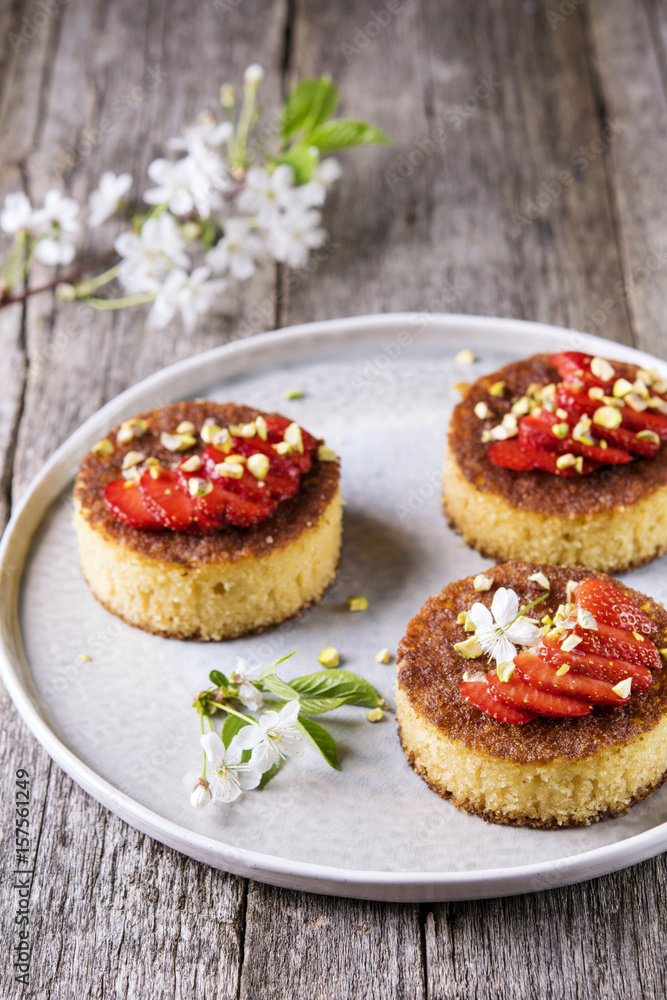 Pieces of homemade semolina cake with strawberry and pistachio decorated flowers of cherry on a rustic vintage wooden table. Selective focus Pieces of homemade semolina cake with strawberry and pistachio decorated flowers of cherry on a rustic vintage wooden table. Selective focus