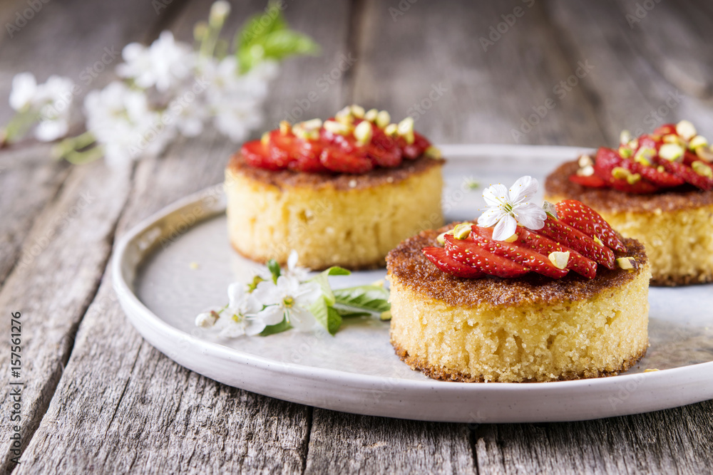 Pieces of homemade semolina cake with strawberry and pistachio decorated flowers of cherry on a rustic vintage wooden table. Selective focus Pieces of homemade semolina cake with strawberry and pistachio decorated flowers of cherry on a rustic vintage wooden table. Selective focus