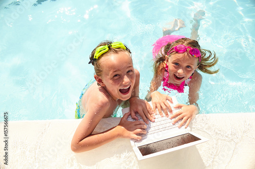Happy little boy and girl using laptop in pool