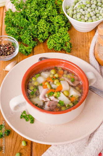 Chicken soup with green peas and vegetables in a bowl on a wooden background