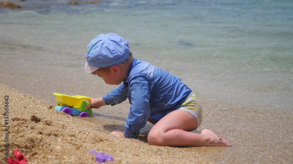 A child plays with sand and toys on the beach on a sunny hot day A child plays with sand and toys on the beach on a sunny hot day