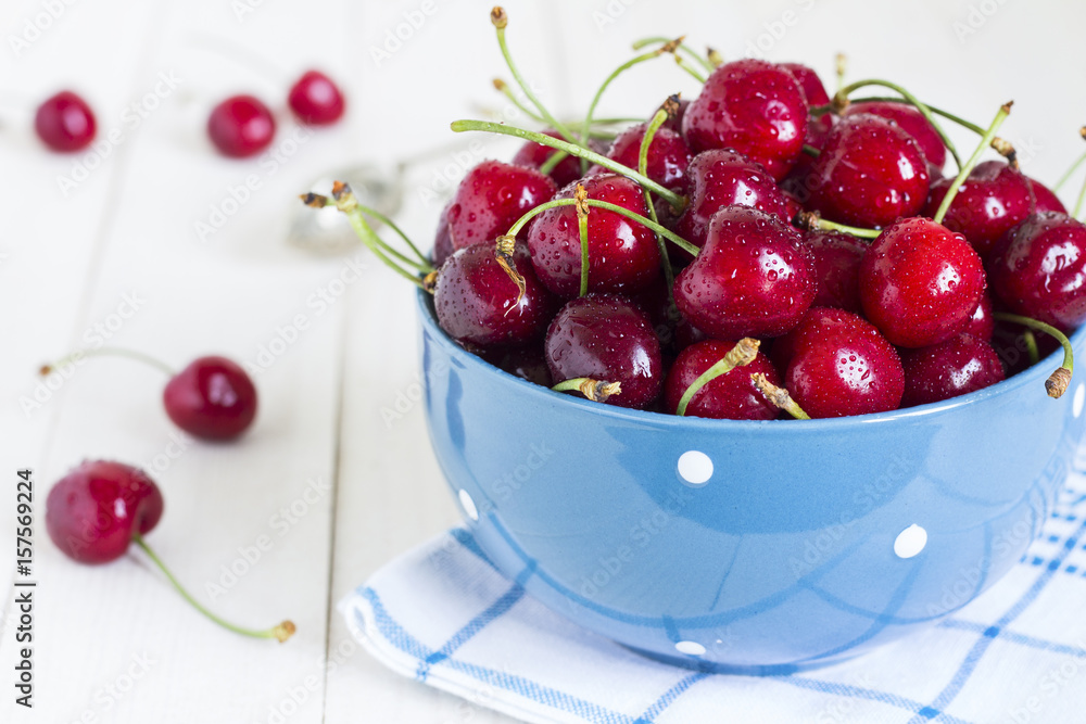 Red cherries in bowl on white wooden background on blue towel Red cherries in bowl on white wooden background on blue towel