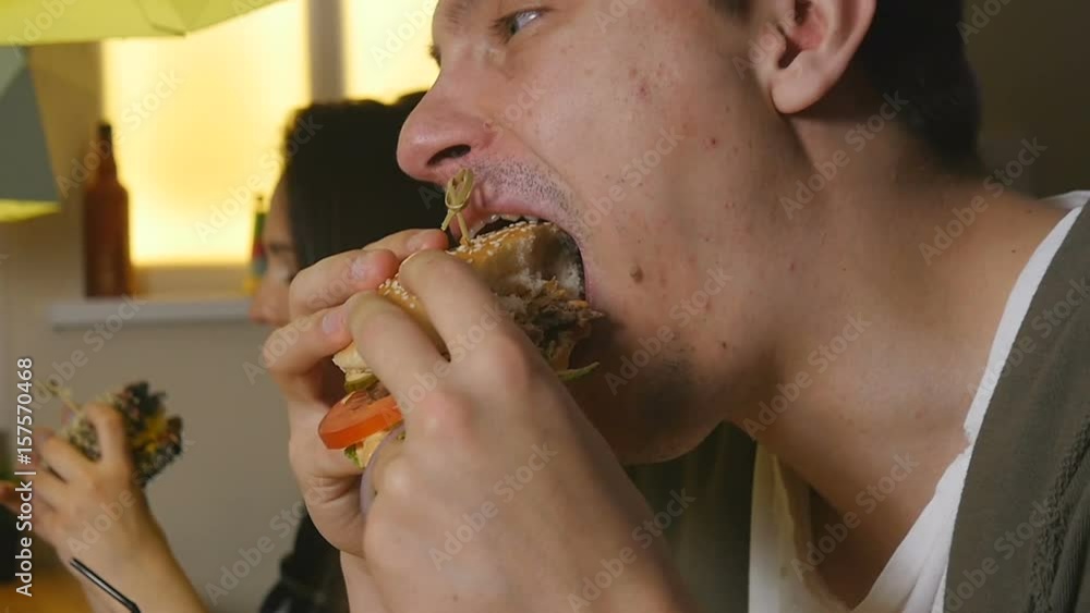 Closer up man bites and eats burger at a cafe