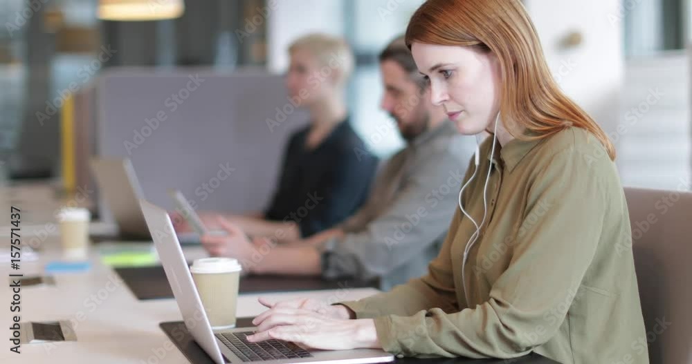 Businesswoman working on laptop with headphones in an open plan office Businesswoman working on laptop with headphones in an open plan office