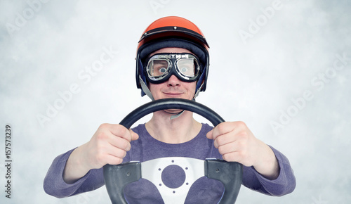 Fototapeta Naklejka Na Ścianę i Meble -  Man in red helmet and goggles with steering wheel. car driver concept