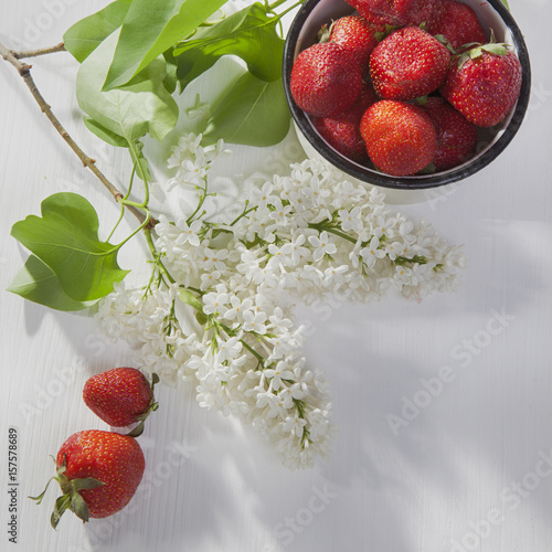 the Strawberry in an aluminum cup, white lilac on a white napkin on a white wooden table photo