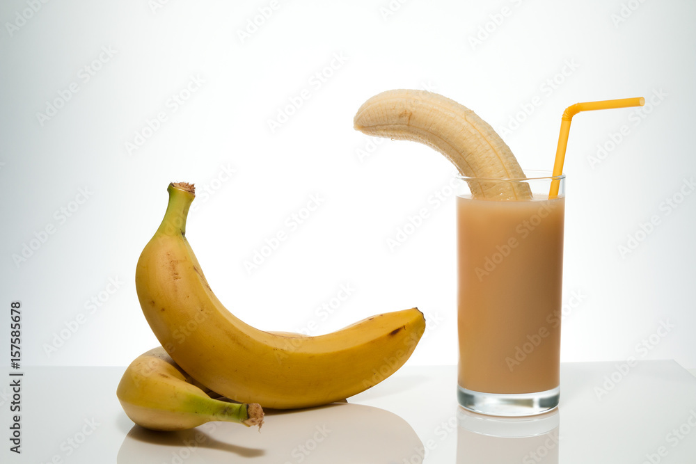 Healthy food and vitamins: a cleared ripe yellow banana in a glass with banana juice with a cocktail straw, and bananas on a table on a white background with space for text