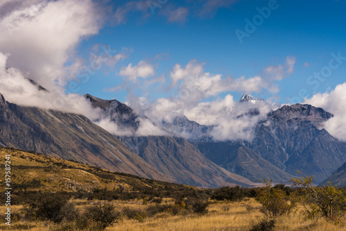 Middle Earth, New Zealand - March 14, 2017: Snow capped High mountain range around Rock of Middle Earth under blue sky with white clouds. Set in a high desert mountainous scenery.