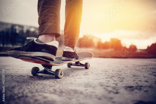 A boot of a skateboarder's shoes is standing on a skateboard ride in the sunset on the road, close-up. Concept street sports in leaky boots