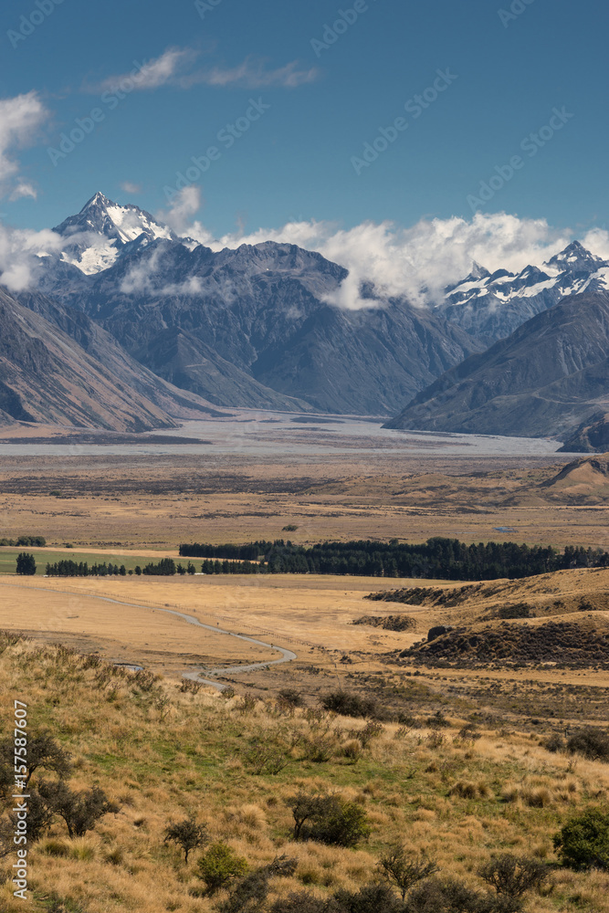 Middle Earth, New Zealand - March 14, 2017: Closeup Portrait of Meandering shallow Rangitata River among snow capped high mountains. Dry high desert scenery near Edoras under blue sky, white clouds.