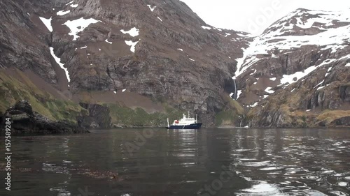 Ship near waterfall in rocky coast and mountains of Falkland Islands. Beautiful background of amazing nature. Unique natural phenomenon of Antarctica.