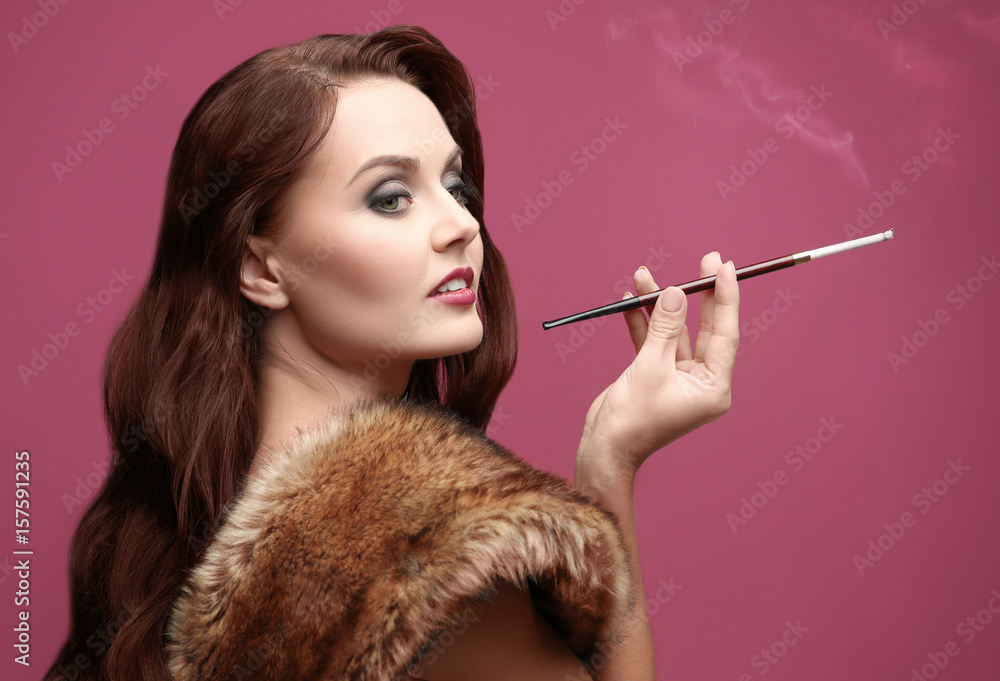 Obraz premium Beautiful woman smoking cigar on color background