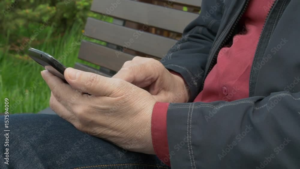 Elderly Man Sitting On Park Bench And Messaging On Mobile Phone Elderly Man Sitting On Park Bench And Messaging On Mobile Phone