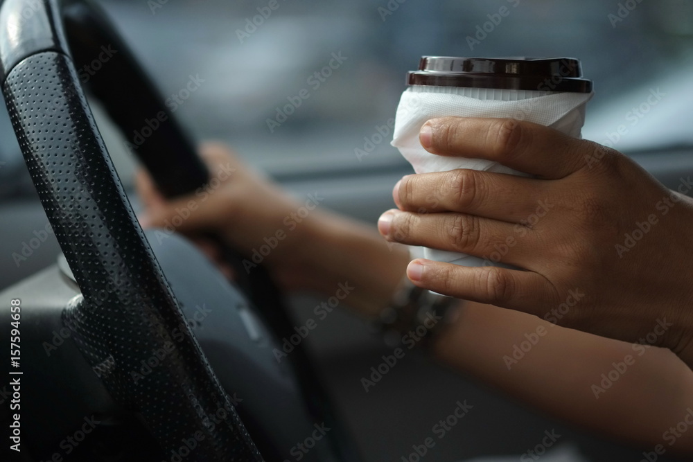 Obraz premium A woman holding a coffee mug with the other hand holding a steering wheel while driving a hurry.